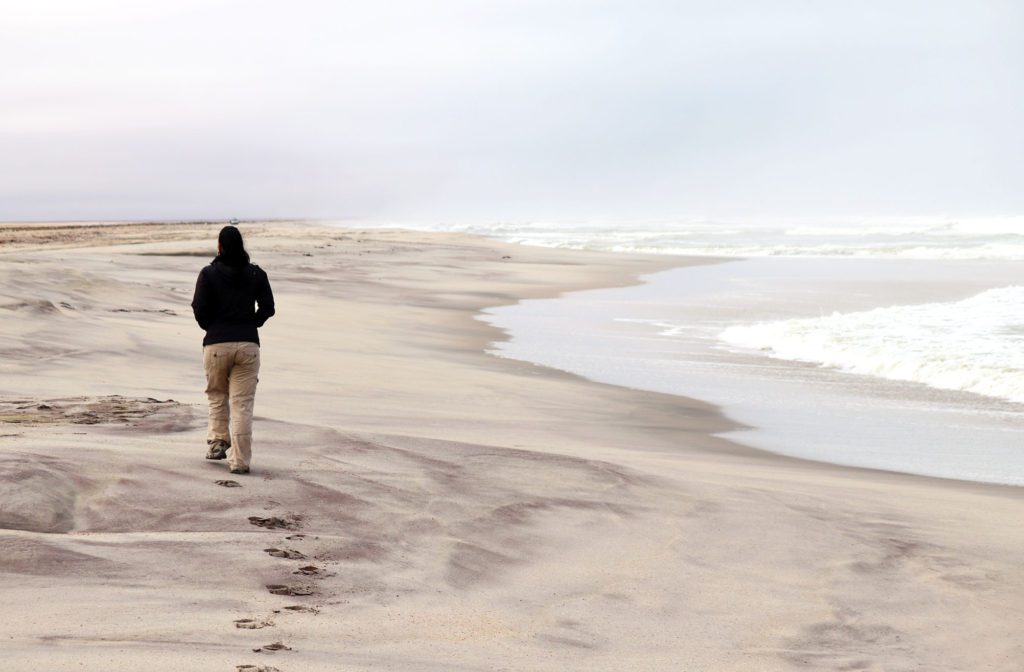 Robyn walking down a deserted beach in Namibia. The weather is cloudy and dull, which represents her feelings and desire for a change.