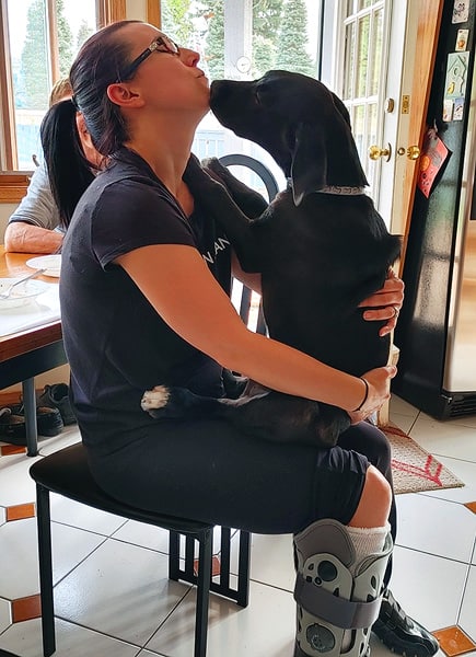 Robyn sitting on a chair with her dog. There is a cast on her leg after breaking her foot in 2021.
