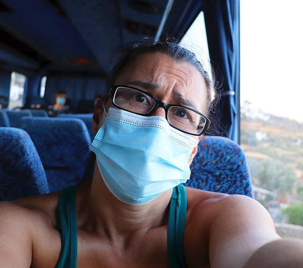 Robyn sitting on a bus with a face mask in Greece with a distressed look on her face.