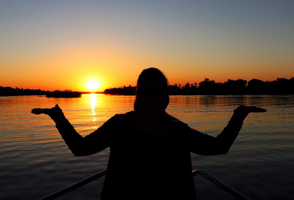 Sailing down the Zambezi river at sunset. Robyn is in silhouette with arms up and confused.