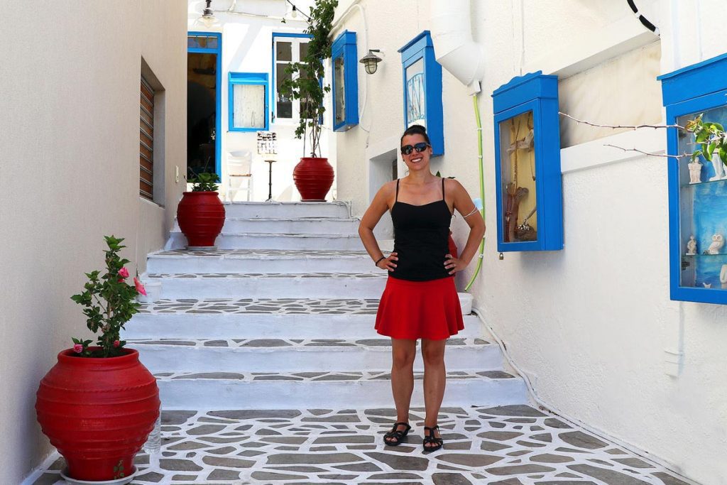 Robyn standing on steps in a cute white and blue alley on Milos, Greece. This was the beginning of the heat wave in the summer of 2021.
