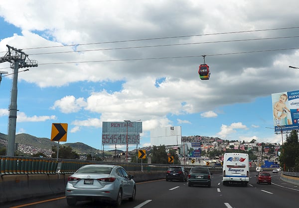 The 3 lane highway as it approaches the city of Pachuca. There is a gondola overhead transporting people from one area of town to the next.