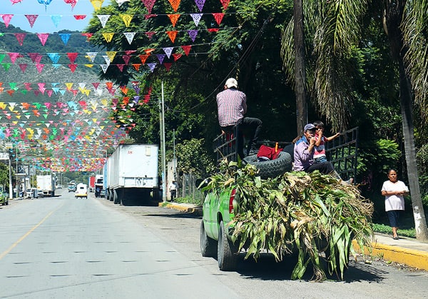 A truck packed with corn husks, carrying 3 people in a small town in Mexico.