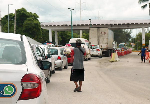 A vendor selling drinks and snacks on the side of the road near a construction site. There is a long line of cars and a bridge up ahead.