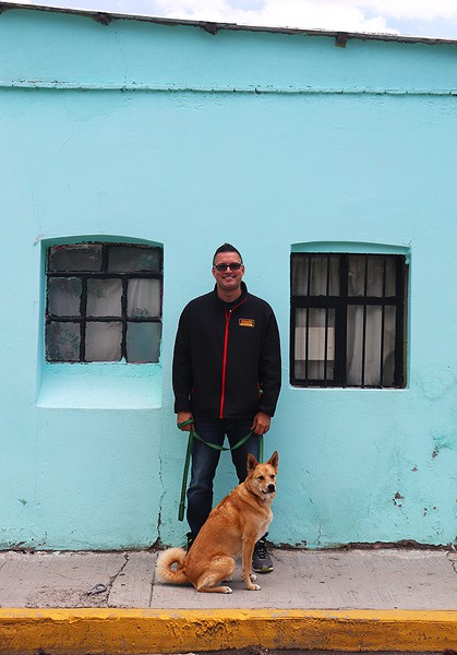 Gavin and our dog Leonardo standing in front of a colorful blue wall.