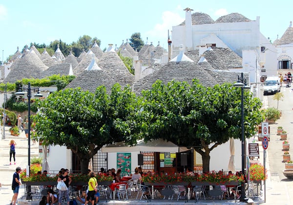 An outdoor café shaded with large green trees in the town of Alberobello,