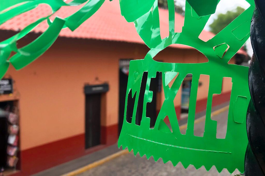 A close up of a Mexico streamer hanging from the second story window overlooking a quiet street in the town.