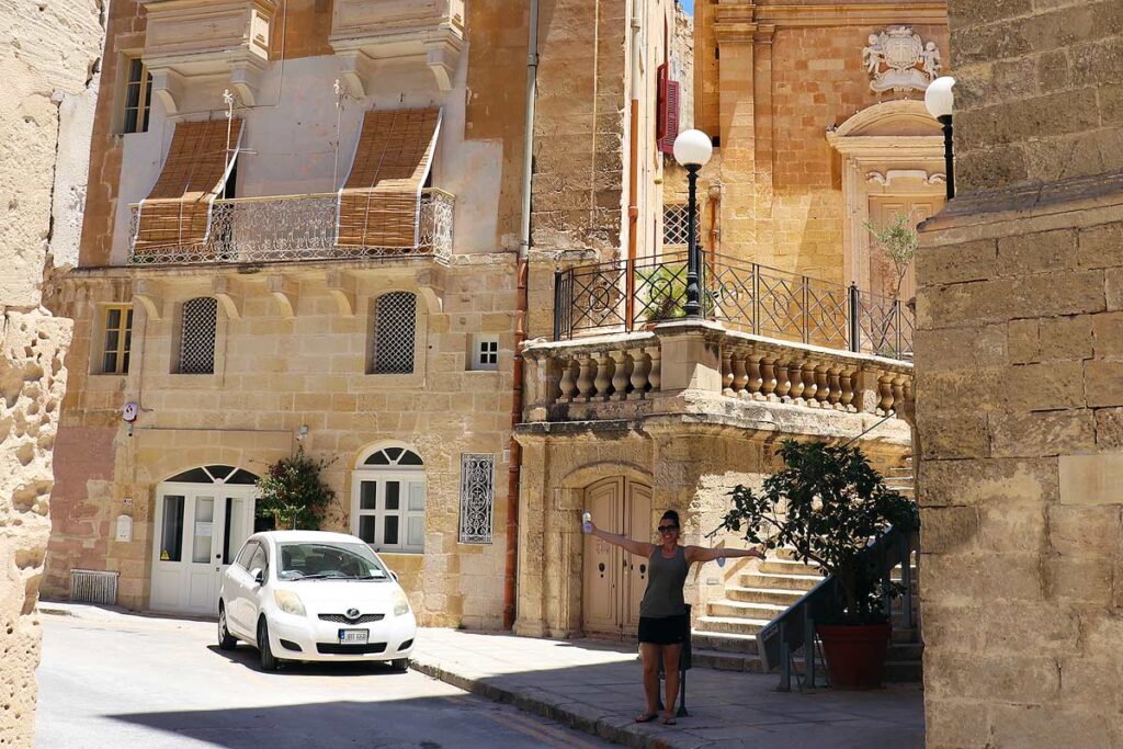 Robyn standing with her arms stretched on the left side of the road in the 3 Cities. Driving in Malta can be easy if you follow the rules.