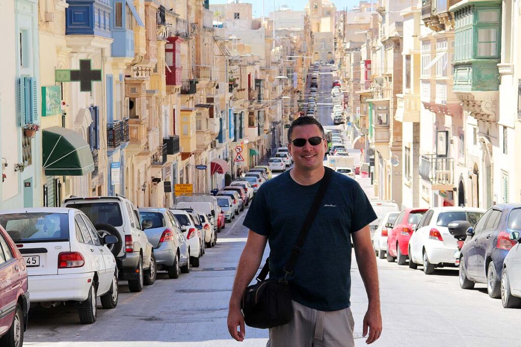 Gavin standing on a street in Valletta surrounded by parked cars in front of beautiful buildings.