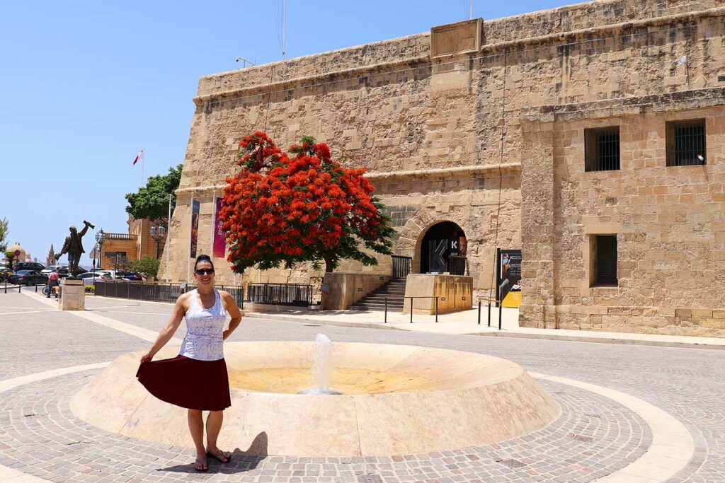 Robyn standing in front of a red tree in her red skirt in beautiful Malta.