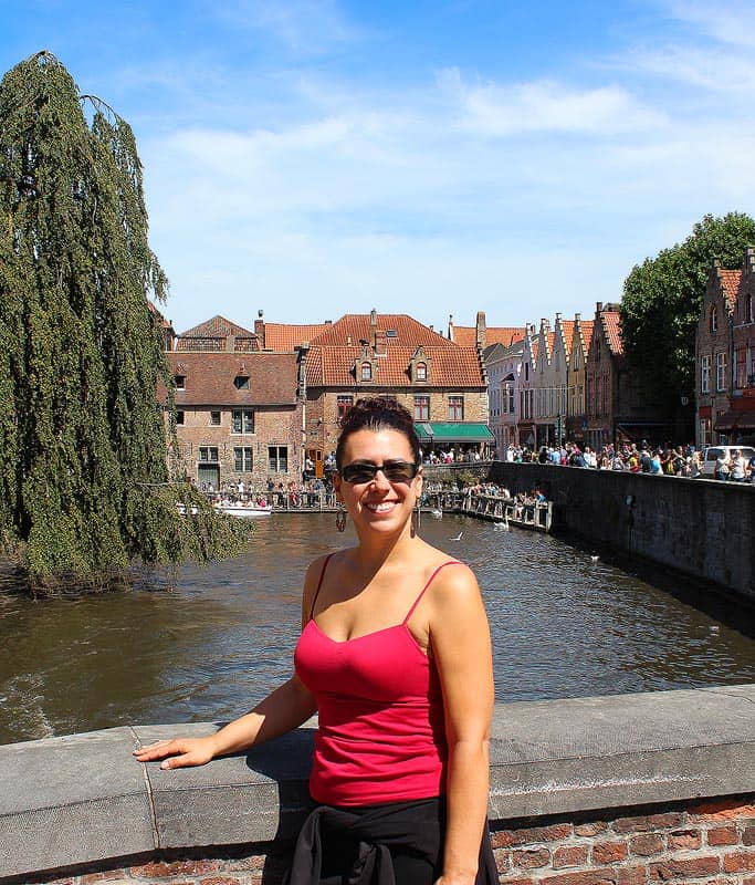Robyn wearing a bright red tank top standing in front of a quiet canal in Bruges, one of the best towns to visit on your Netherlands and Belgium itinerary.