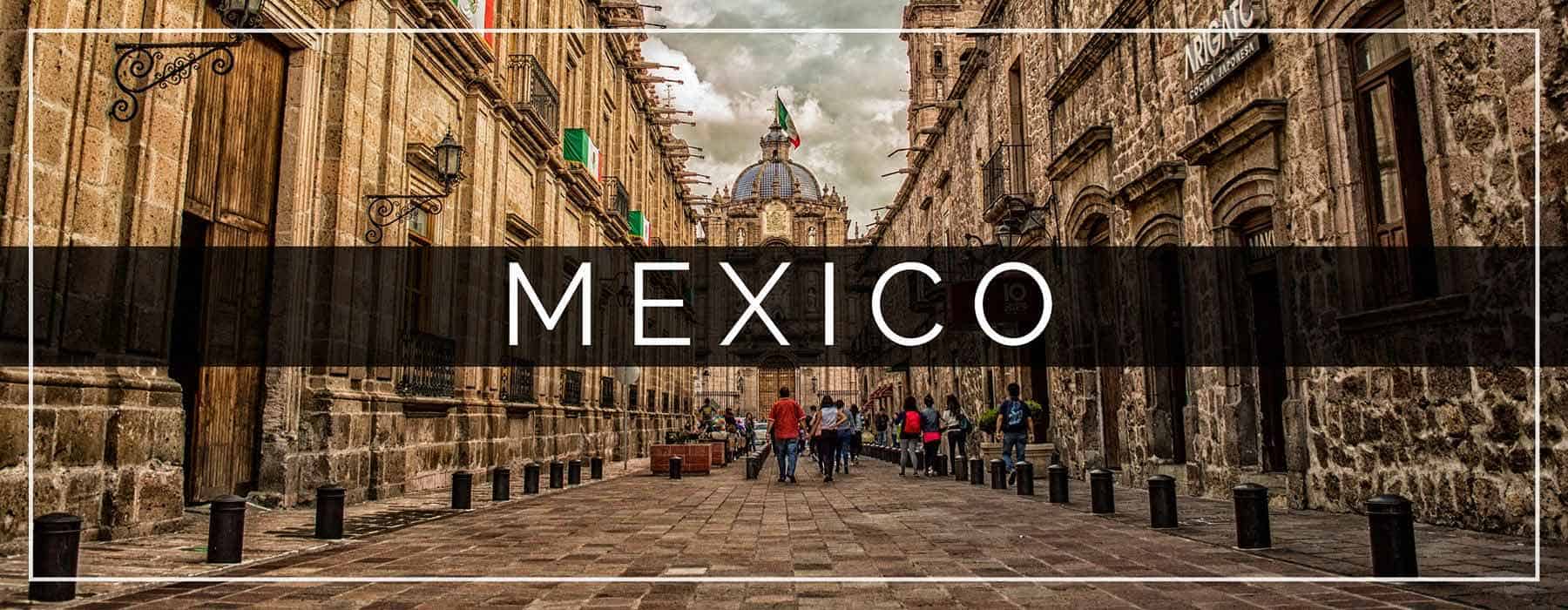 Mexico Header with a picture of two beautiful historical buildings in Morelia, Mexico. The picture is symmetrical with a gorgeous cathedral at the end. Mexican flags are hanging on the left building and people are walking in the center. The word Mexico is in large white letters over a faded black bar in the center.