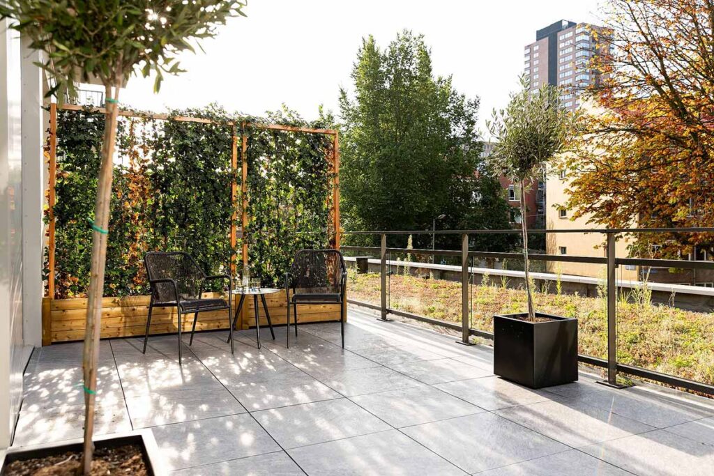 The spacious terrace at the Fletcher Boutique Hotel Slaak-Rotterdam furnished with two chairs, a small table, a planter and a divider wall covered in greenery.