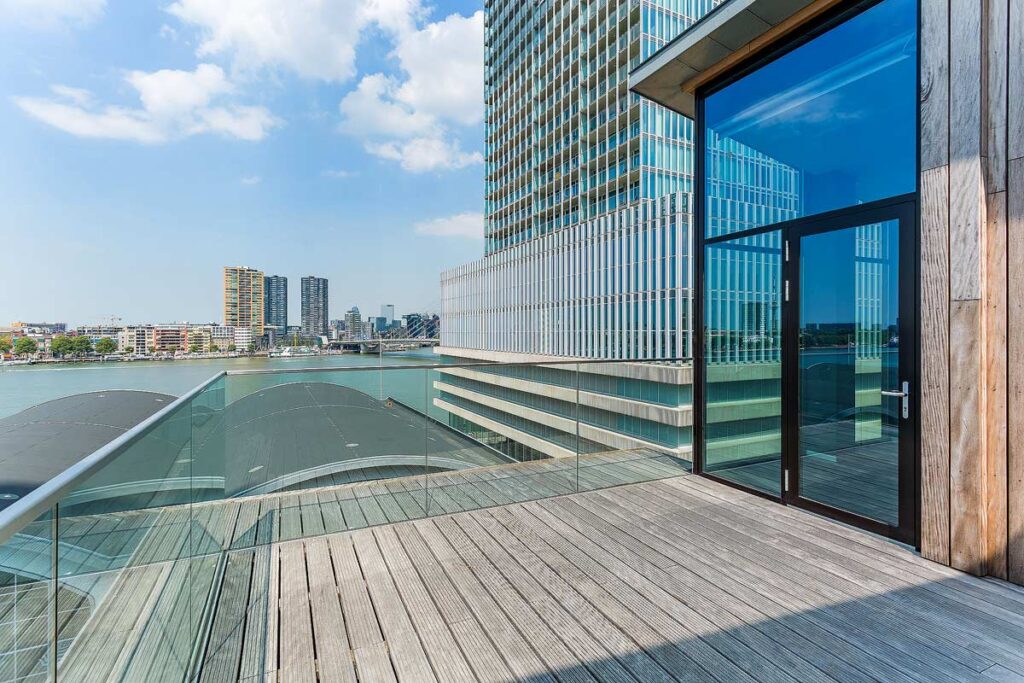The large terrace with city and water views at the Room Mate Bruno hotel in Rotterdam. There is a glass door on the right leading to the balcony, and downtown buildings in the distance across the water.