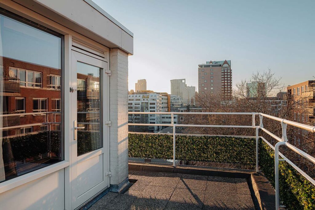 The spacious balcony lined with green bushes at the Savoy Hotel Rotterdam overlooking the city.