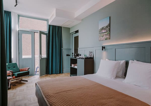 A suite at the Supernova Hotel, one of the best Rotterdam Hotels with Balcony. The suite has teal wainscotting, a large bed and modern finishes, with 2 open doors leading to the private terrace.