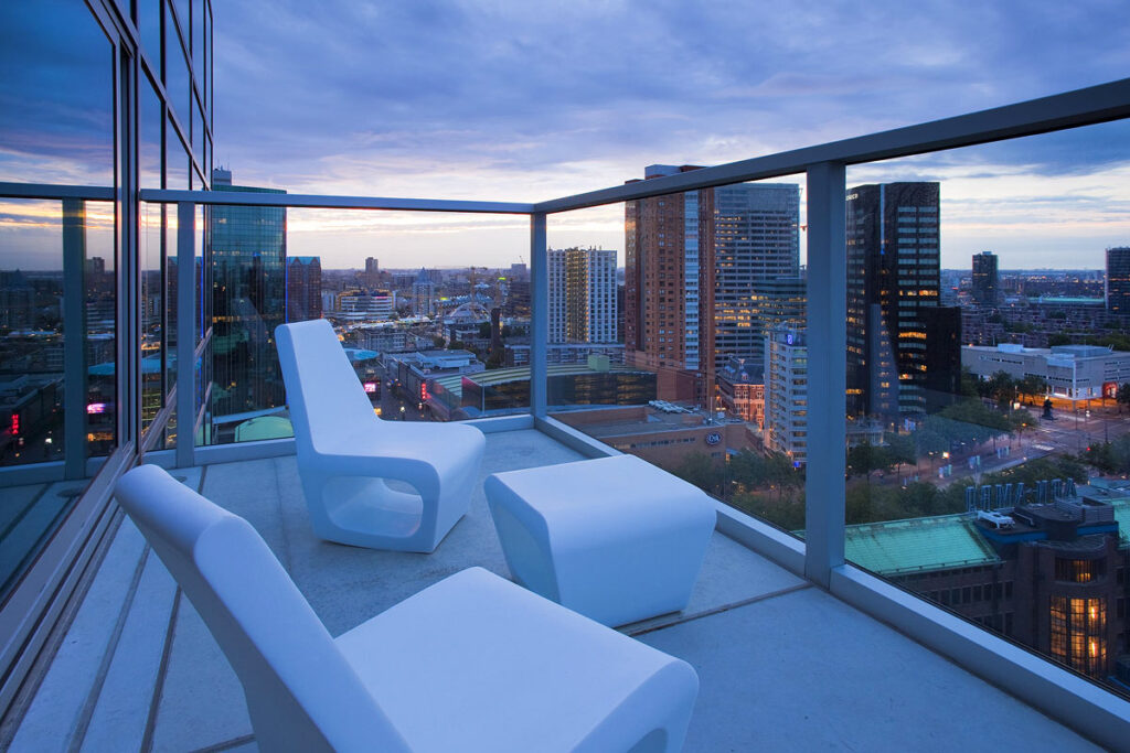 A panoramic view of the city skyline at evening from a spacious balcony with modern furniture on a high floor at Urban Residences, one of the best Rotterdam hotels with balcony.