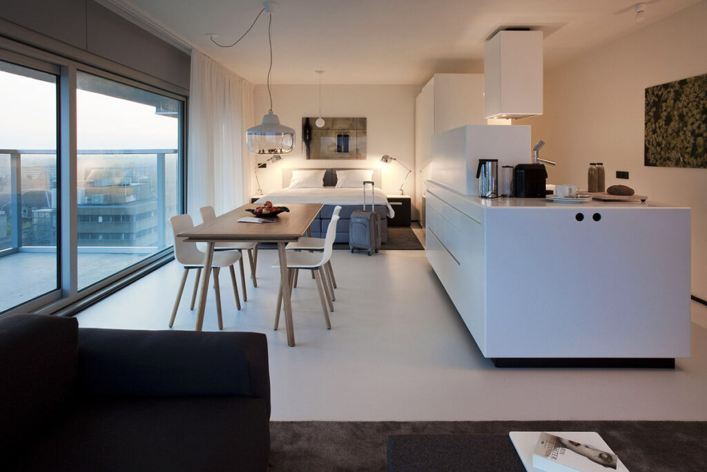 The interior living space featuring a couch, fully kitchen with large table and queen bed on the far wall. Urban Residences are the best option is you want a Rotterdam hotel with balcony and additional living space.