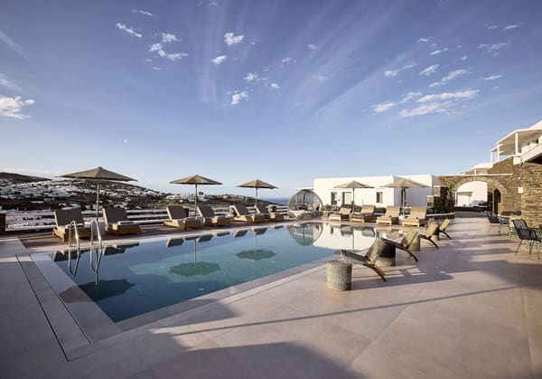 The gorgeous pool at Nivel Boutique Hotel, one of the best Sifnos hotels with a pool in Apollonia. The long pool is surrounded by loungers and umbrellas. There is a white building at the far end and you can see the landscape in the distance.