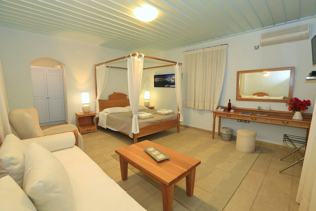 A very large suite at Petali Village Hotel, one of the best Sifnos hotels with a pool in Artemonas. The rooms has wood furniture including a poster bed, nightstand, couch, coffee table and vanity.