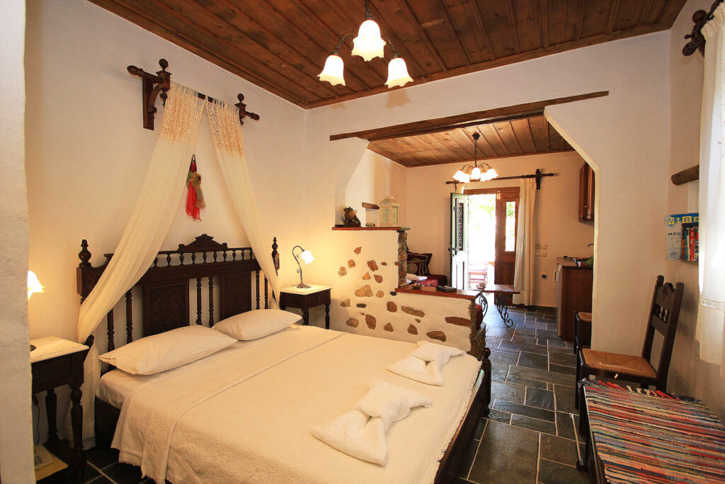 A suite at Sifnaika Konakia, one of the best traditional Sifnos hotels to stay at. This large suite has a king sized bed with traditional wood furniture. There are wood ceilings and an exposed brick dividing wall to the living space.