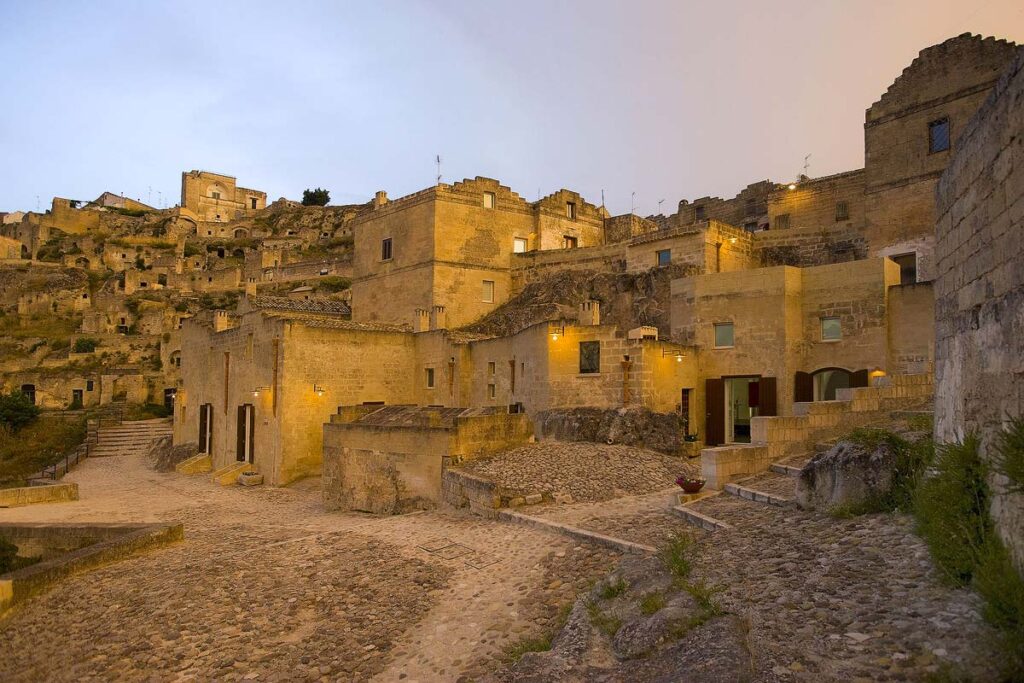 A view of the Basiliani Hotel in Matera, one of the most unique towns in Pugia to visit. Set in the historic center, this hotel is made of rock and built into the earth and lit with pretty lights at dusk.