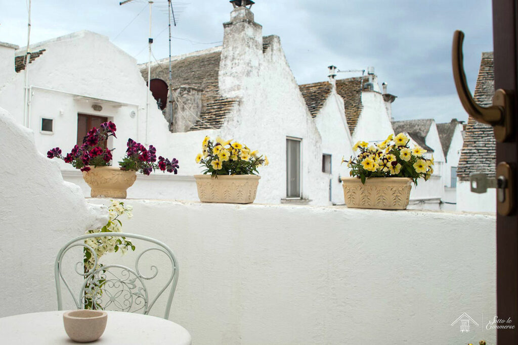 A lovely terrace with a small table, single chair and colorful flowers overlooking trulli houses at the Sotto le Cummerse Albergo Diffuso, one of the best places to stay in Locorotondo,