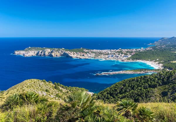 An aerial view of a beach in Kalamata Greece. There are green shrubs in the foreground, and gorgeous turquoise water surrounding the sandy coastline.