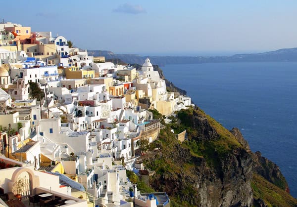 A view of Santorini, one of the most popular islands to visit in Greece. You can see the stacked white houses and churches on the edge of the cliff with the blue sea below.
