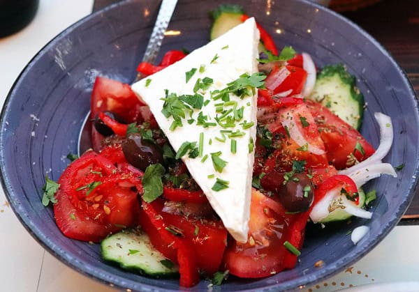 A delicious bowl of Greek salad with juicy red tomatoes, cucumbers, olives and a slab of feta cheese sprinkled with fresh oregano. Yes, Greek food is Mediterranean!
