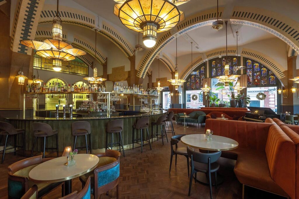 The gorgeous lounge in the Clayton Hotel, an accessible hotel in Amsterdam. Set in a historic building with arched ceiling, elegant chandeliers and a large bar on the left with spacious seating on the right.