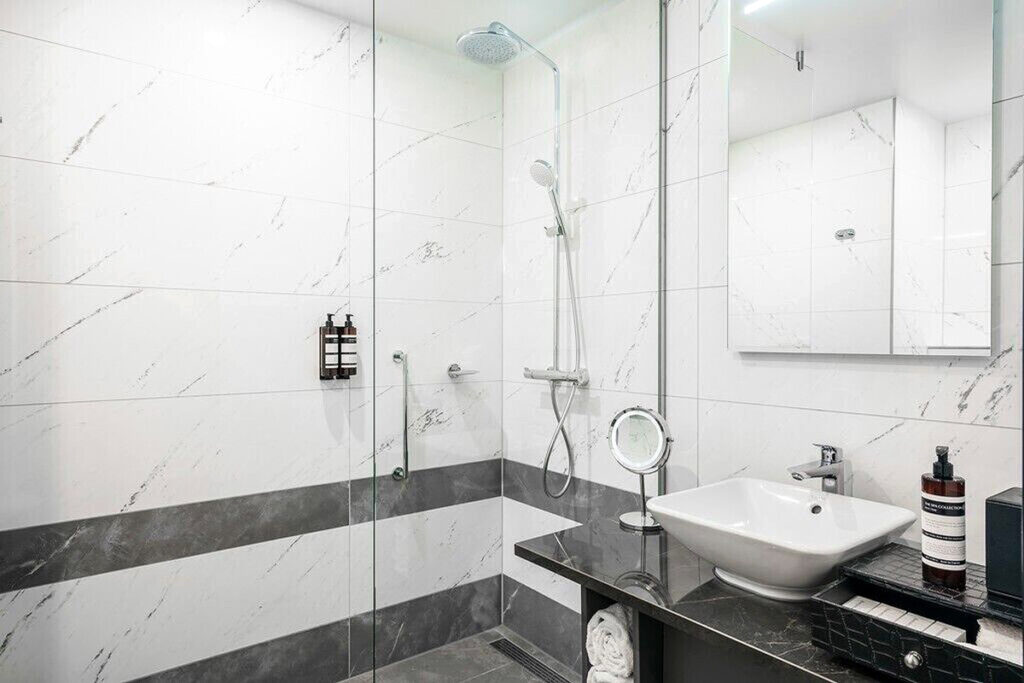 A roll-in shower with lowered shampoo on the wall with a lowered sink and portable mirror at the Monet Garden Hotel Amsterdam. It is one of the best wheelchair friendly hotels to stay at with a canal view.