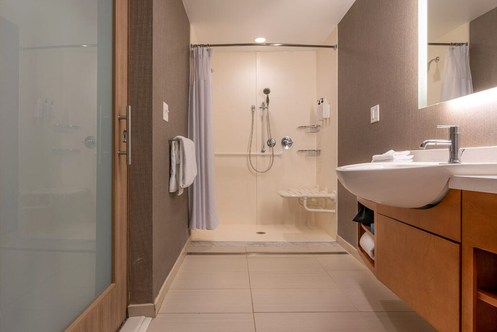 A wheelchair accessible bathroom with a roll-in shower and attached shower seat and grab bar. The sink and vanity are also lowered.