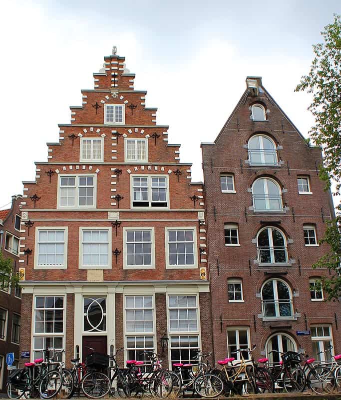 Two traditional Dutch brick houses with beautiful details and pointed roofs. There are pink flower boxes in front of the houses.