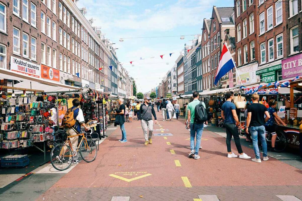 A busy shopping street in Amsterdam, including the Albert Cuypmarkt, is free thing to do in the city. This pedestrian only street is full of people walking and browsing the many shops under a blue sky.
