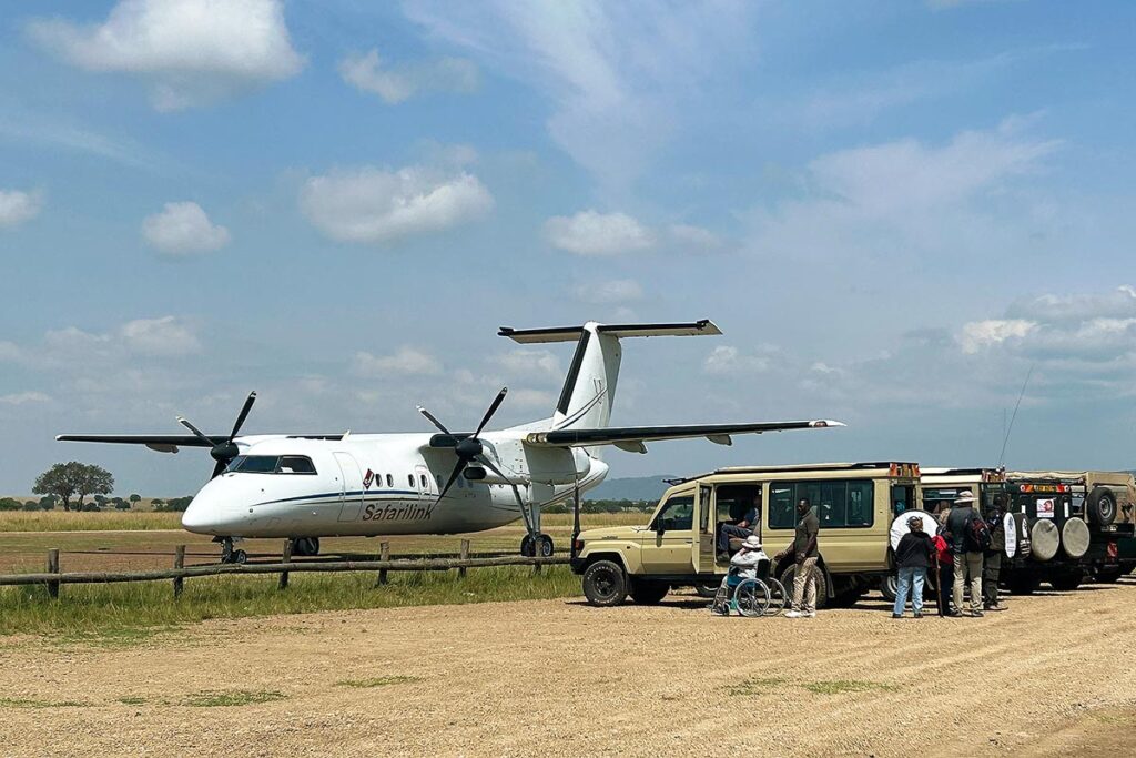The Safarilink plane sitting on the runway in Masai Mara with our safari jeeps lined up picking up travelers, including wheelchair users.