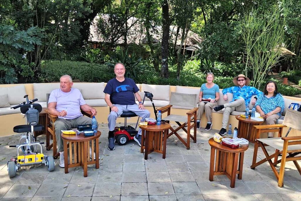Our May 2026 accessible Kenya safari group relaxing on a day without any game drives in order to recharge. They are sitting outdoors in a semi circle with trees behind them.