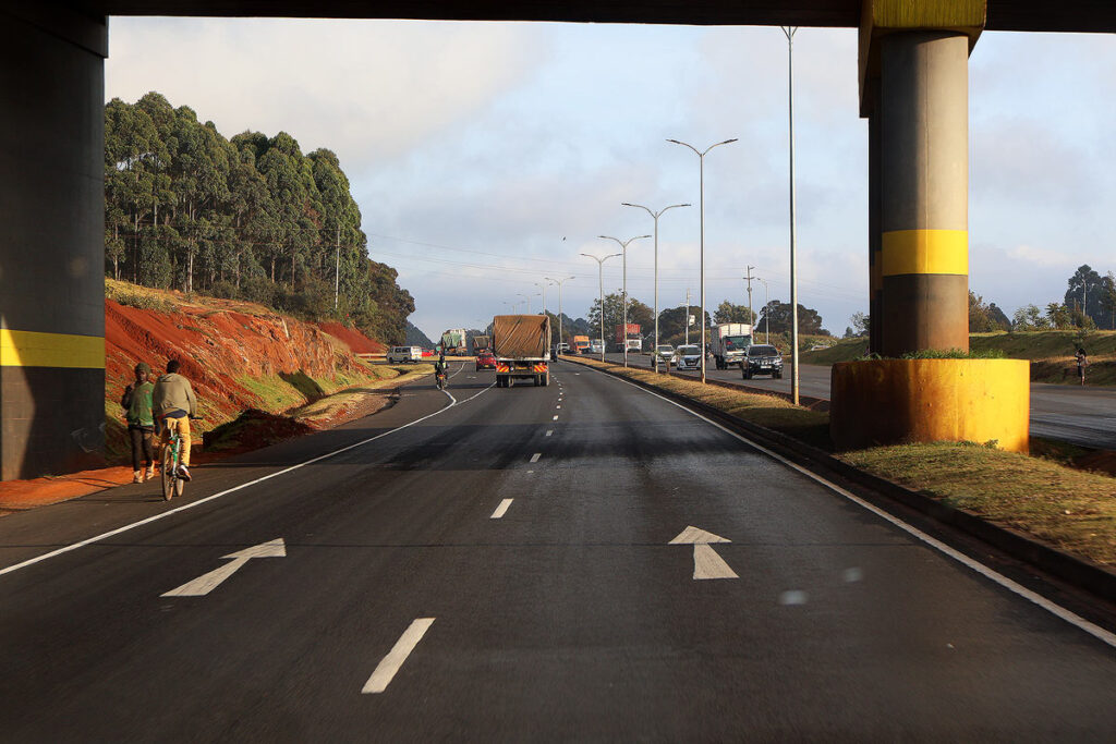 A paved highway with two lanes indicated by arrows in Kenya with an overpass above.