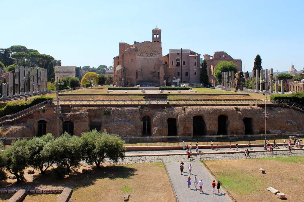 An expansive view of the ruins at the Roman Forum with a few people exploring the grounds under a clear blue sky. This is one of the best things to do with limited mobility in Rome.
