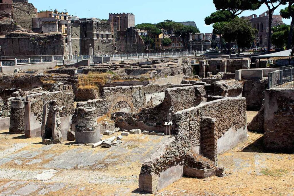 Ruins of ancient Rome at the Roman Forum, one of the popular things to do in Rome with limited mobility. There are half broken walls and columns scattered throughout with trees and taller structures in the distance.