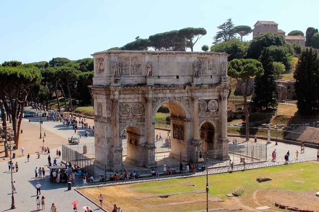 The Arch of Constantine outside the Colosseum in Rome with people at its base and green trees behind.