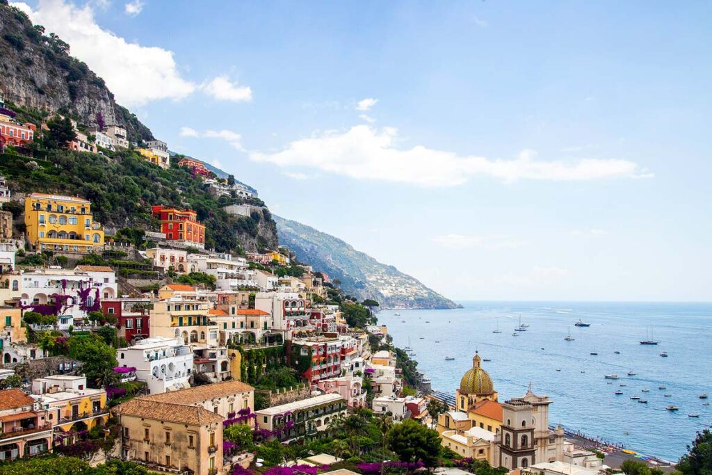 The beautiful town of Amalfi along the Amalfi Coast with colorful buildings sprinkled along the green mountains with the sea below.
