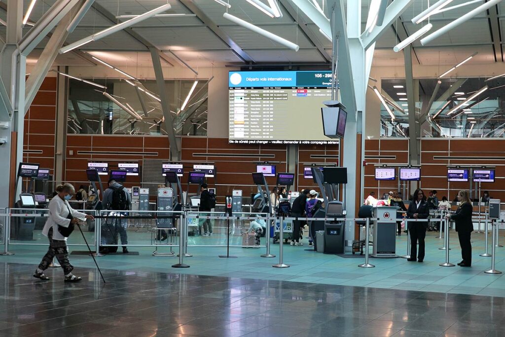 A woman with a cane walking through the empty Vancouver International Airport with check in counters behind her.
