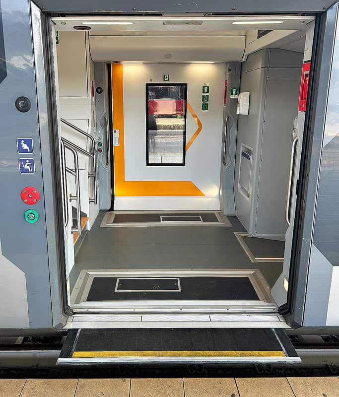 A train car on TrenItalia with open doors showing the width and space of the car fit for a wheelchair user. There is a short step ramp that extends from the car to shorten the gap and assist wheelchair users when boarding.