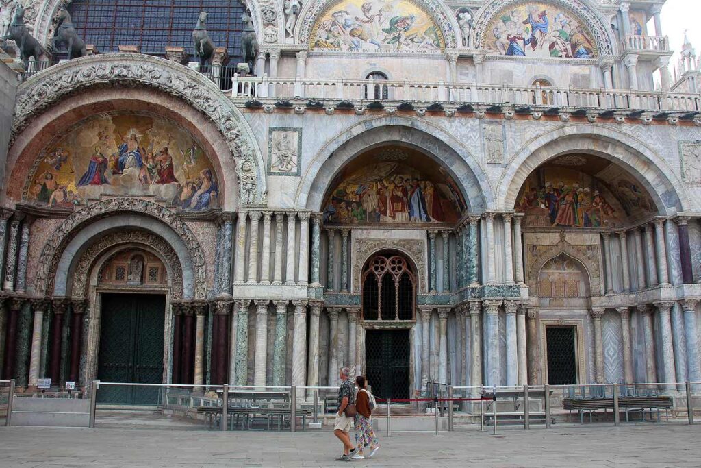 A couple of tourists walking in front of beautiful St. Mark's Basilica in the early morning before the crowds arrive, a smart choice on a Venice day trip.