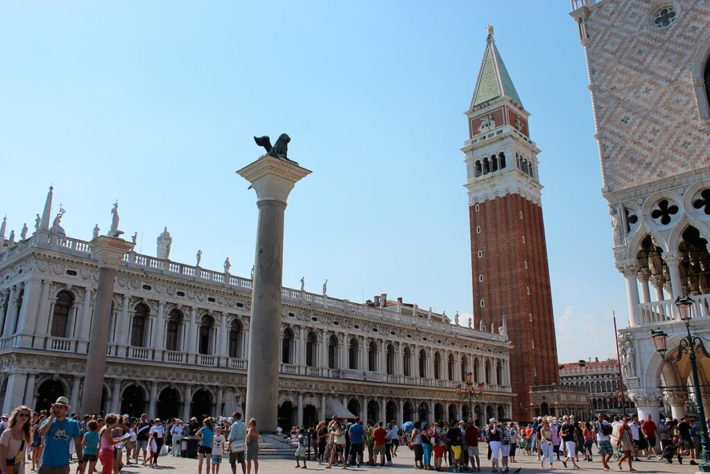 Crowds of people visiting on a day trip to Venice's San Marco Square. The brick Campanile behind in the right and Doge's Palace on the left.