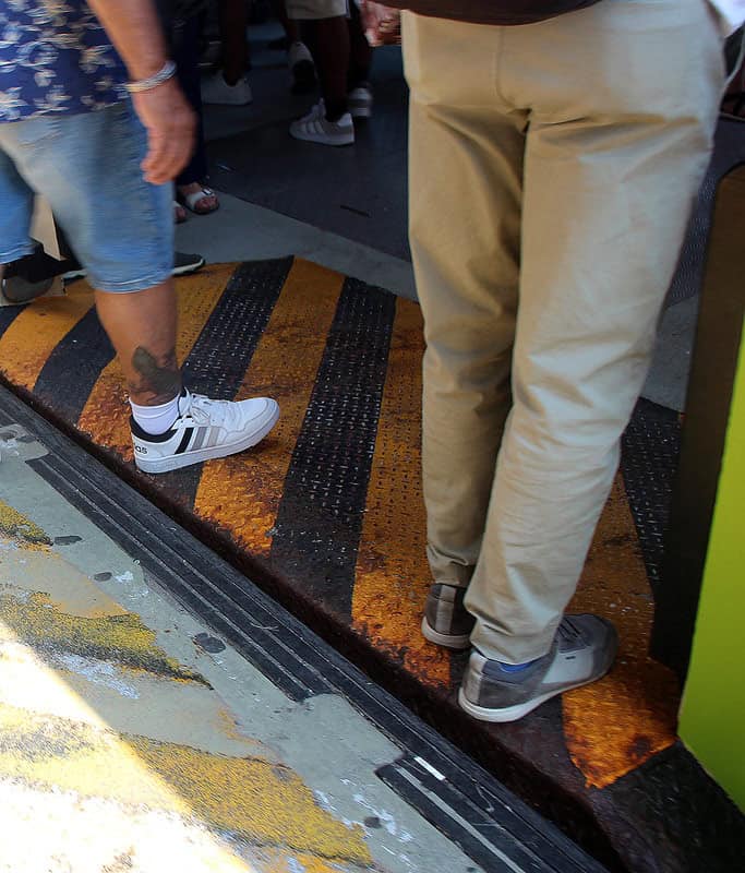 A close up of a Vaporetto platform perfectly lined up to a water bus in Venice. You can see two men's legs, one in khaki pants and one in jean shorts getting onto the boat.