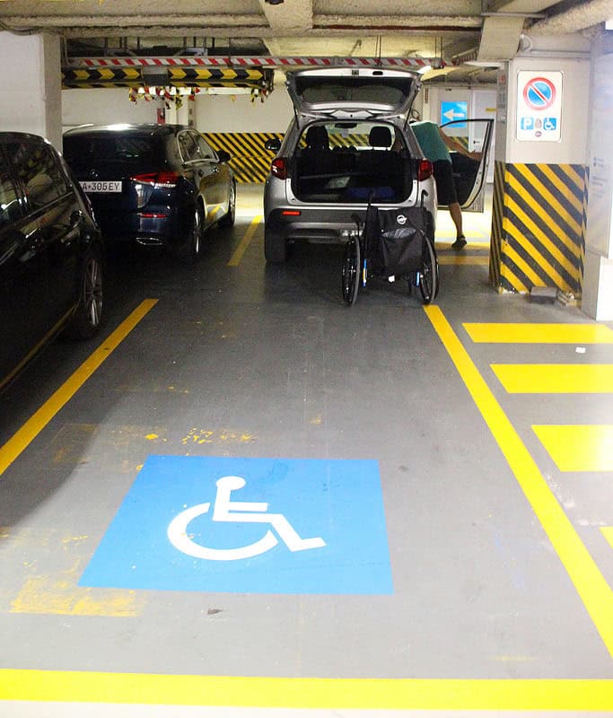The two wheelchair parking spots in the San Andrea Garage, perfect for spending one day in Venice with a wheelchair. There is a blue wheelchair logo painted on the floor and our sliver rental car in the second stall. My wheelchair is in front of the trunk and Gavin is packing up.