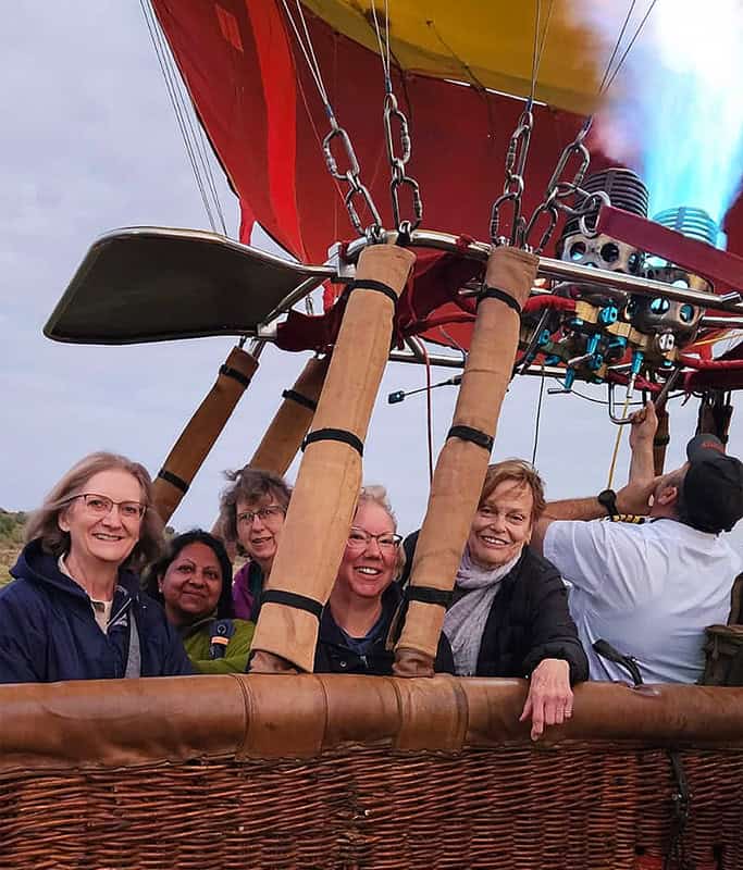 Mary standing in the balloon in Masai Mara with other participants of the accessible Kenya safari. They are smiling as the balloon is starting to lift off the ground.